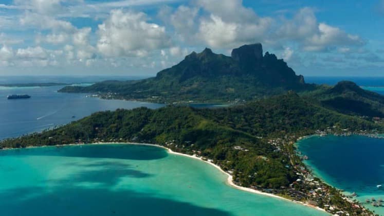 Aerial view of Bora Bora's iconic Mount Otemanu rising above turquoise lagoons and white sand beaches.