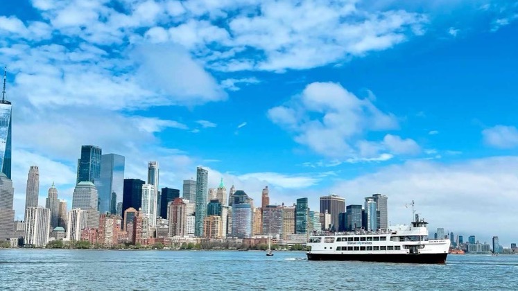 A passenger ferry cruises across New York Harbor with the Lower Manhattan skyline in the background