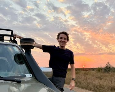 Gianmaria holding to a Toyota Land Cruiser with a sunset in the background